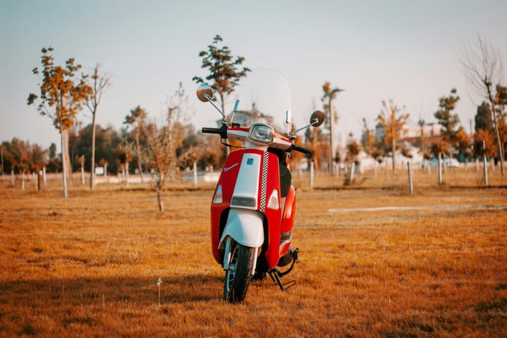 Red Vespa scooter parked on dry autumn grass under a clear sky.